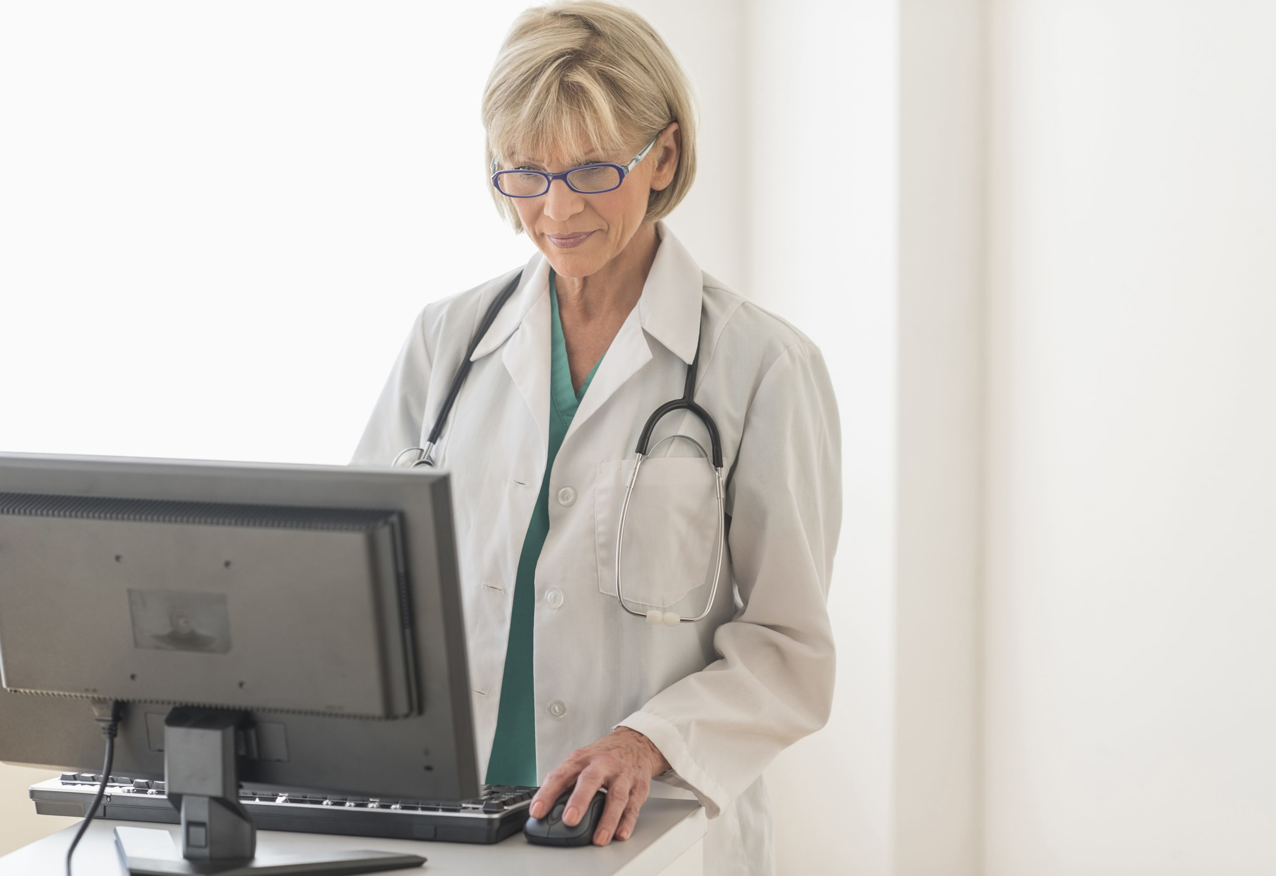 Female Doctor Using Desktop PC At Desk